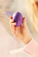 An Easter egg painted in purple in the hand of a child on a Sunny morning. It is Easter morning. Selective focus.