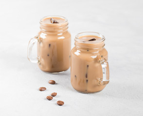 Cold coffee with milk and ice in a jar on a light background 