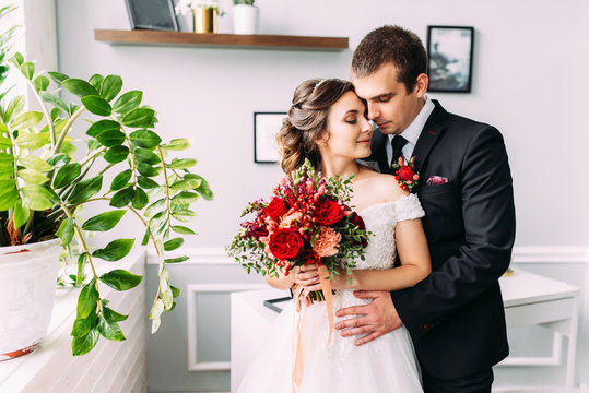 Beautiful wedding couple. Luxurious dress of the bride and stylish suit of the groom. Wedding bouquet of peony roses, wedding accessories, studio photo shoot