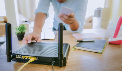 closeup of a wireless router and a man using smartphone on living room at home ofiice, equipment for  working from home, while in quarantine isolation during the Covid-19 health crisis.
