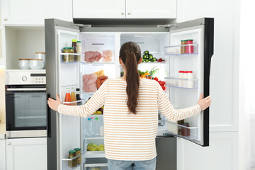 Young woman opening refrigerator in kitchen, back view
