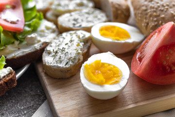 cut eggs andandwiches for healthy snack/lunch. Hard boiled eggs and sandwiches with cream cheese, tomatoes, lettuce on the wooden board. Layout decision in close up