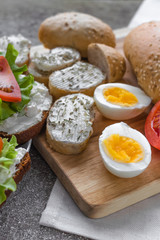 cut eggs andandwiches for healthy snack/lunch. Hard boiled eggs and sandwiches with cream cheese, tomatoes, lettuce on the wooden board. Layout decision in close up