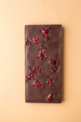 A bar of milk chocolate with dried cranberries on a brown background top view. The concept of minimalism.