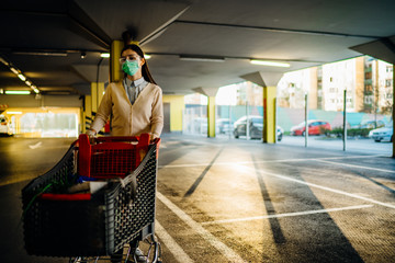 Woman wearing mask groceries/supplies shopping in supermarket,pushing trolley.Food supplies shortage.Panic buying and hoarding.Empty parking garage.Sustainable coronavirus shopping restrictions