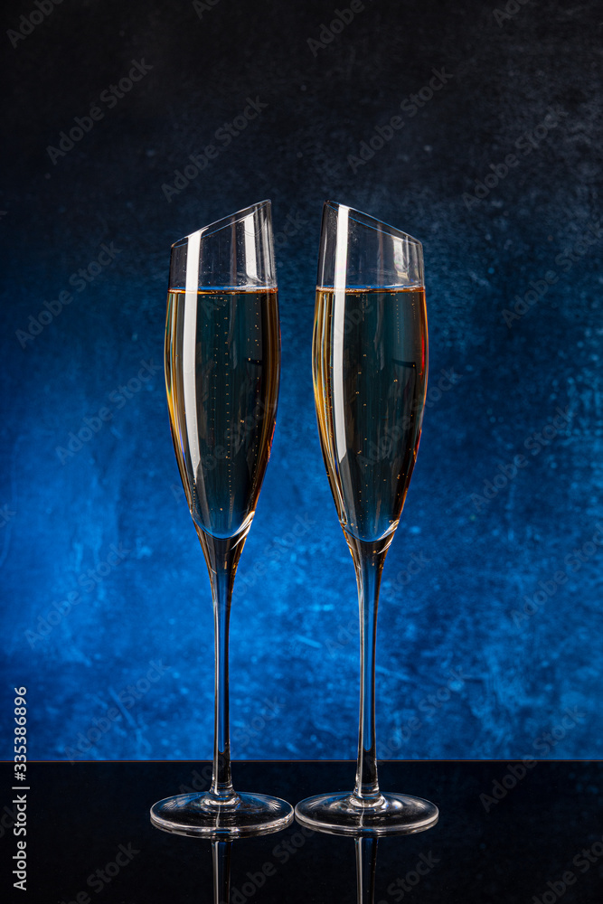 Wall mural two glasses with champagne on a black mirror surface. blue background concrete wall. black glass. cr