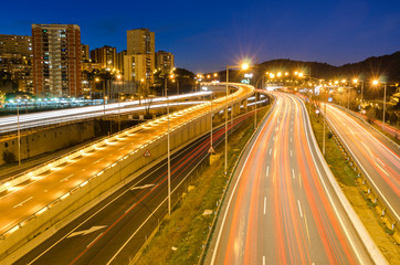 Fototapeta na wymiar Paisaje urbano de la entrada de la autopista a Barcelona de noche. con los rastros de las luces de los coches 