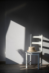 white chair with a hat cylinder on background of the wall with a shadow from the window