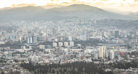 Aerial view to Tbilisi city buildings from far distance with caucasus mountains in the background. 2020