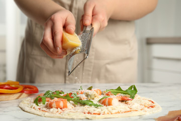 Woman grating cheese onto pizza at white marble table, closeup