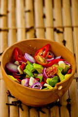 Fresh salad with avocado, tomato, onion and chili in wooden bowl on a bamboo table.