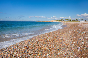 Fototapeta na wymiar Beautiful seascape with calm sea, pebbles beach, blue sky of suburb in South Athens located in the Athens Riviera, Greece.