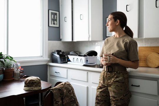 Thoughtful female soldier in camouflage drinking coffee in kitchen