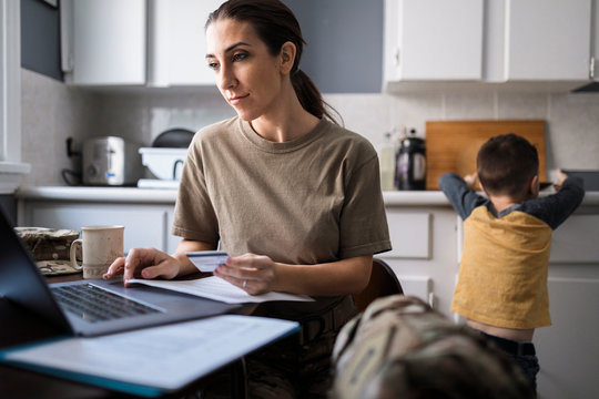 Female soldier paying bills at laptop in kitchen