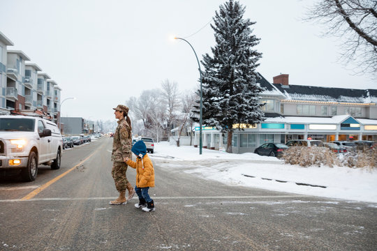 Soldier mother and son holding hands crossing snowy street