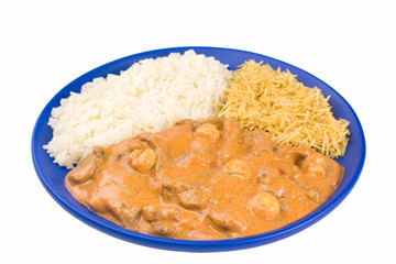 Brazilian tenderloin stroganoff with rice and potato sticks in a blue plate isolated in white background