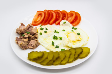 Delicious fresh tuna with eggs, tomatoes, cucmbers with green onion at the morning. Healthy and diet breakfast with tuna, eggs and vegetables on the white plate against white background
