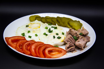 Delicious fresh tuna with eggs, tomatoes, cucmbers with green onion at the morning. Healthy and diet breakfast with tuna, eggs and vegetables on the white plate against dark background