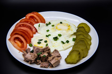 Delicious fresh tuna with eggs, tomatoes, cucmbers with green onion at the morning. Healthy and diet breakfast with tuna, eggs and vegetables on the white plate against dark background