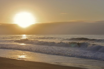 Sun going down on the Atlantic ocean with surfer on the bottom right