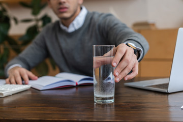 Cropped view of businessman taking glass of water in office
