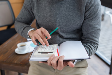 Cropped view of businessman with pencil and notebook using calculator in office
