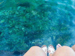 Pies con sandalias blancas en el agua verde turquesa de la costa de Croacia, verano de 2019