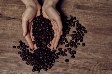 Coffee beans in hands on dark background