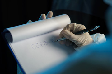 Woman wearing protective hazmat suit  (PPE) and writing virus infected patient's laboratory report.
