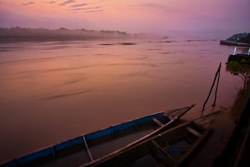 Beautiful, misty early morning sunrise over Rio Huallaga, Yurimaguas, in the Peruvian Amazon region. The pink, purple and orange light color the picture. Typical wooden fisher boats are in foreground.