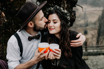 Beautiful young couple enjoying picnic time in evening. They drinking tea and sitting in a meadow.