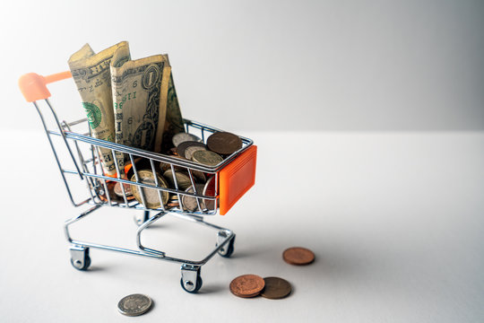 Dollars and other currencies filling up shopping trolley, isolated on white background. To illustrate the financial and economic fluctuations and challenges during covid 19 crisis.