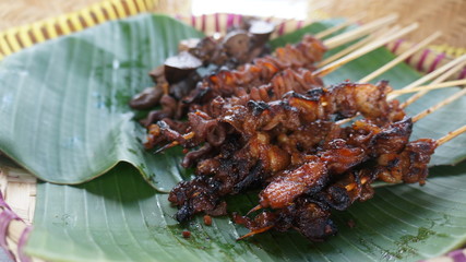 a couple of chicken skewers on a tray lined with banana leaves