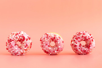 Three fresh donuts with pink icing stand on a pink background. The concept of unhealthy delicious food. Bakery products. Place for text