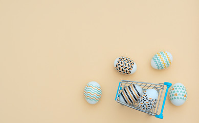 Decorated Easter eggs lie in the shopping trolley on yellow background with blurred Easter eggs. Happy Easter holiday and spring concept. Greeting, invitation card. Flat lay style with copy space.
