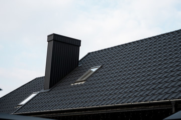 Black metal tile roof. Roof metal sheets. Modern types of roofing materials. Roof of the house, metal roof tile against the blue sky. Building. © Volodymyr_sh