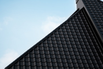 Black metal tile roof. Roof metal sheets. Modern types of roofing materials. Roof of the house, metal roof tile against the blue sky. Building. © Volodymyr_sh