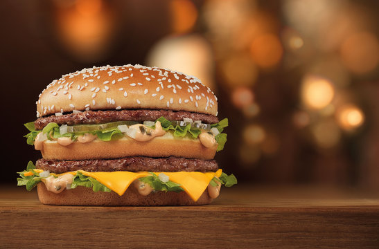slender tall double burger with meat and cheese on a wooden table with bokeh on the background