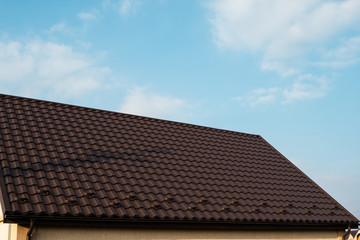 Brown metal tile roof. Roof metal sheets. Modern types of roofing materials. Roof of the house, metal roof tile against the blue sky. Building.