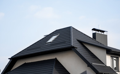Black metal tile roof. Roof metal sheets. Modern types of roofing materials. Roof of the house, metal roof tile against the blue sky. Building. © Volodymyr_sh