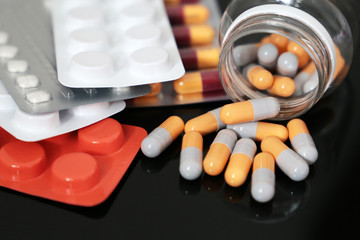 Pills on a dark glass table, medication in tablets and capsules scattered from a bottle. Concept of...