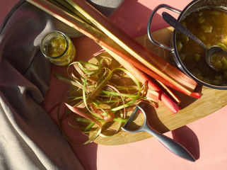 Rhubarb jam, stalks and peel on wooden and pink background. Glass and stainless pot of pieplant marmelade