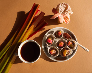 Chocolate balls with rhubarb jam and cup of coffee, on brown background. Pie plant jam and rhubarb bunch.