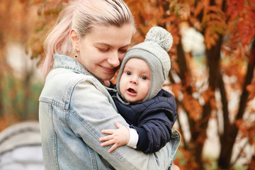 Fototapeta na wymiar A stylish young mother with a small son in her arms walks in the autumn.