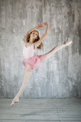Beautiful female ballet dancer jumps on a gray background. Adorable ballerina is wearing a pink...
