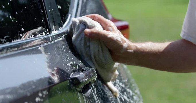 Man hand washing grey SUV car with soapy cloth on hot summer day - close up on soap suds on car