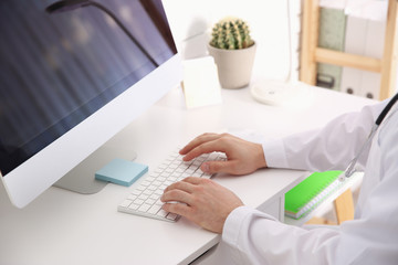 Doctor working with computer at desk in office, closeup