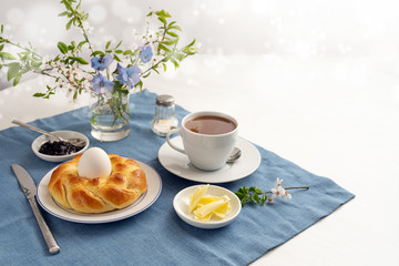 Easter yeast bread nest with an egg, coffee, butter and jam on a blue napkin and a white table, many have to spend the holidays alone during the coronavirus crisis, copy space, selected focus