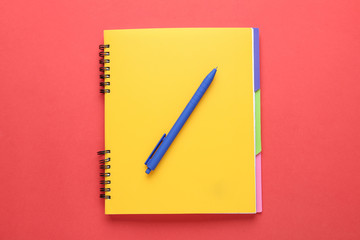 Yellow notebook and pen on red background, top view
