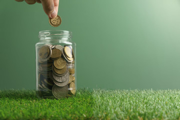 finance conceptual images. male finger insert the coin in the glass bottle of coins on green background. copy space for text. selective focus.